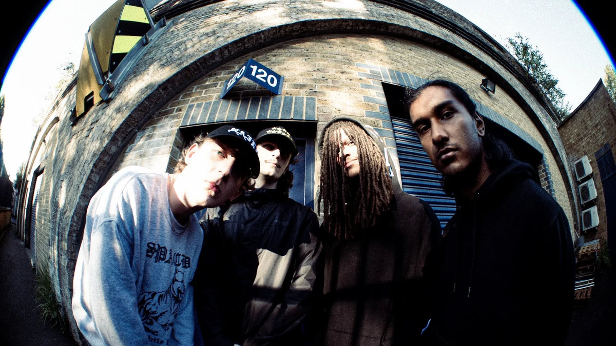 Four members of UK hardcore band So Far So Good pose outside a brick industrial building, photographed with a fisheye lens.