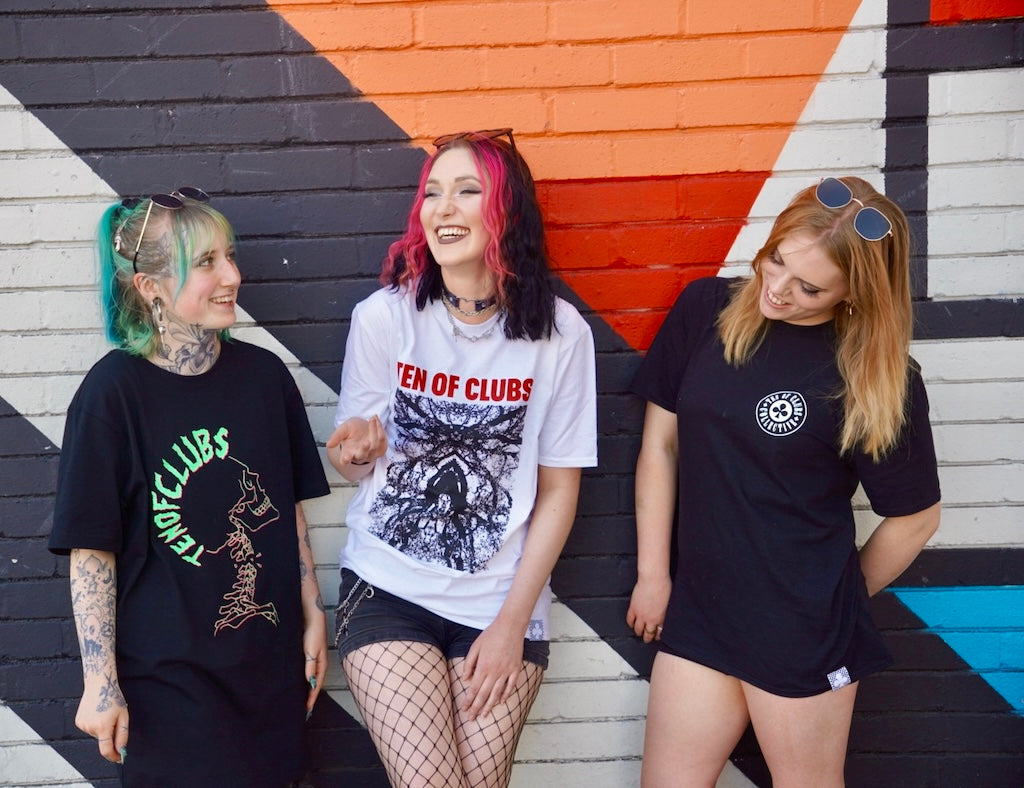 Three women modelling TEN OF CLUBS T-shirts in front of a colourful mural
