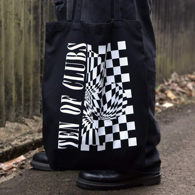 TEN OF CLUBS Wave Tote Bag in black with graphic artwork on the front, held by a person outdoors.